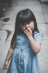 Portrait of girl picking nose while standing on footpath