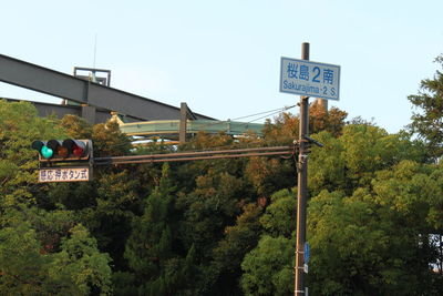 Road sign by trees against clear sky