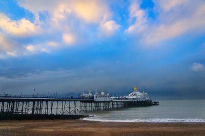 Pier on beach against cloudy sky