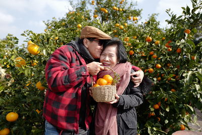 Man holding oranges kissing woman on forehead in orchard