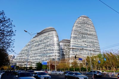 Cars on road by modern buildings against clear sky