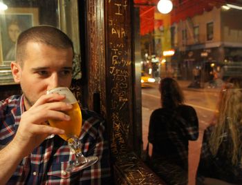 Young man drinking beer while looking out through glass window at restaurant