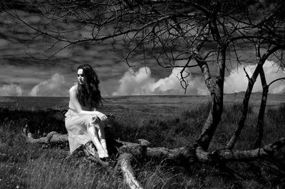 Thoughtful woman sitting on log against sky