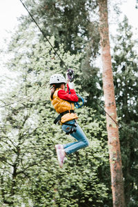 Low angle view of girl zip lining in forest