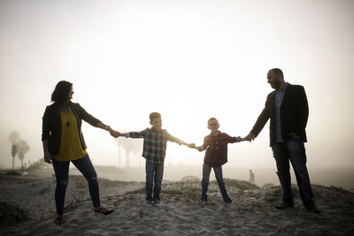 Happy silhouette family holding hands while standing at beach against sky during foggy weather
