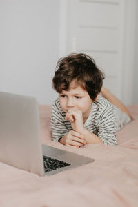 Little boy lie in the bedroom on the bed and look at the laptop. high quality photo