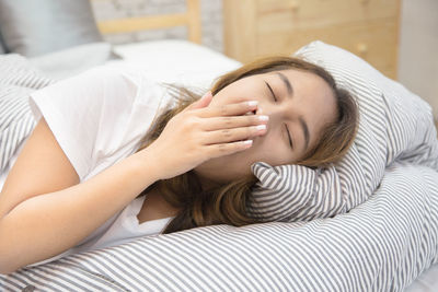 Woman yawning while lying down on bed at home