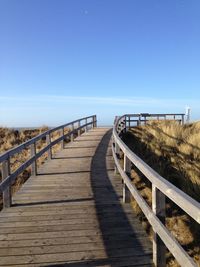 Empty footbridge leading towards sea against sky