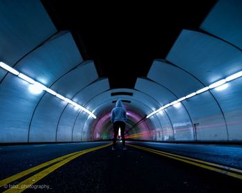 Rear view of man walking in illuminated tunnel