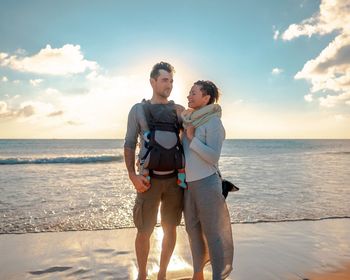 Smiling friends enjoying at beach against sky during sunset