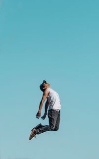 Low angle view of man jumping against blue sky