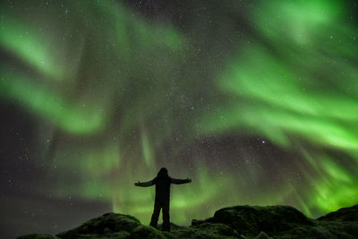 Low angle view of silhouette mature man with arms outstretched standing against northern lights at night