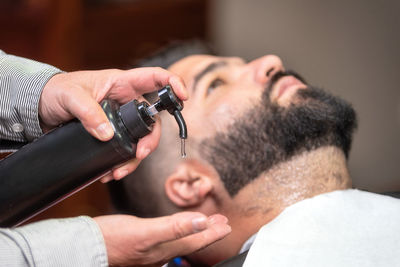 Cropped hands of barber holding cream bottle by customer in salon