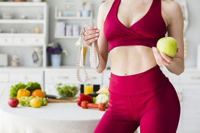 Midsection of woman holding apple while standing in gym