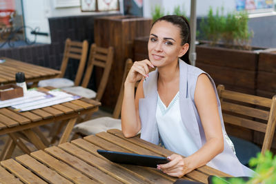 Beautiful businesswoman with smile sitting with touchpad in cozy restaurant