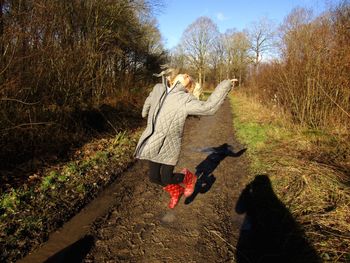 Girl jumping on dirt road amidst bare trees