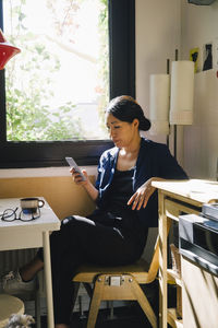 Female architect using smart phone while sitting at desk in home office