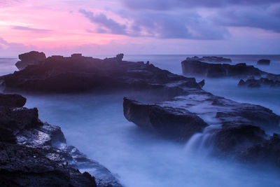 Rocks in sea against sky during sunset