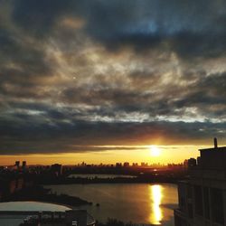 Scenic view of river by buildings against sky during sunset