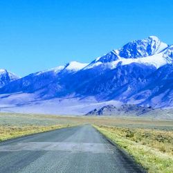 Road amidst snowcapped mountains against clear blue sky