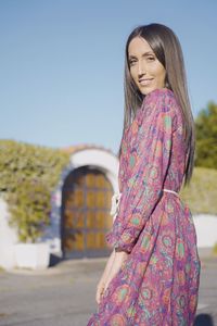 Portrait of smiling young woman standing against clear sky