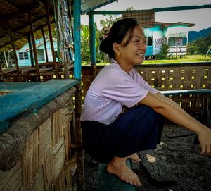 Side view of a smiling woman sitting against built structure