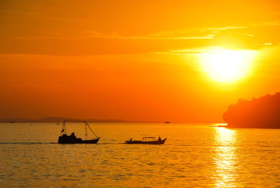 Boats sailing in sea against orange sky