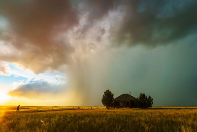 Scenic view of farm and abandoned building  against dramatic stormy sky