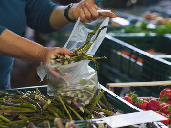 Midsection of woman holding asparagus in crate at market