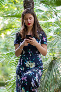 Young woman using phone while sitting on tree