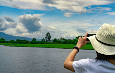 Asian woman use smartphone take a picture of beautiful landscape of river, mountain, and forest.