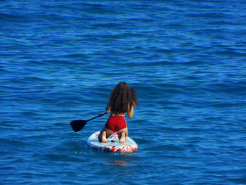 Rear view of woman kneeling on paddleboard in sea