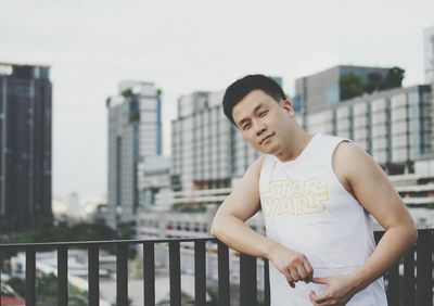 Young man standing on railing against cityscape