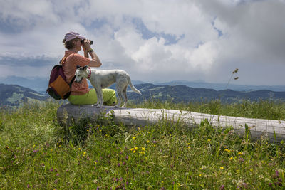 Woman sitting with dog on log against sky