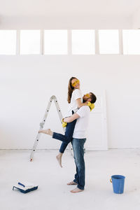 A young couple in love have moved into a new house and are making repairs painting white walls