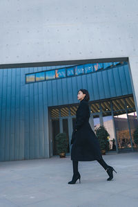 Full length side view of woman walking against building in city