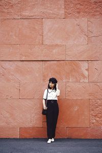 Full length of young woman standing against brick wall