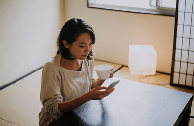 Young woman using phone while sitting on table at home