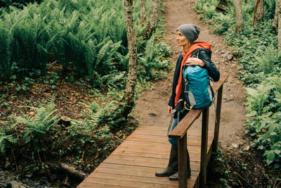 A woman in a raincoat and a hat in the thickets of the forest enjoys the freshness after the rain