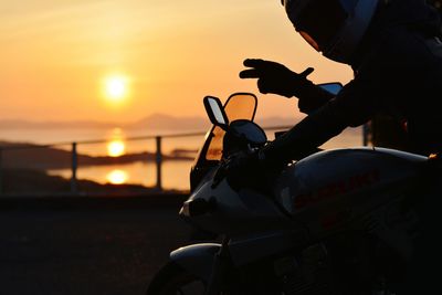 Man riding motorcycle showing peace sign against sky during sunset