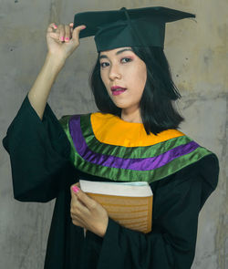 Portrait of young woman holding camera while standing outdoors