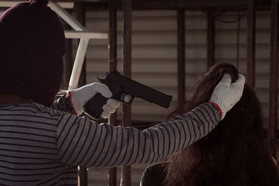 Rear view of burglar holding woman hair and handgun