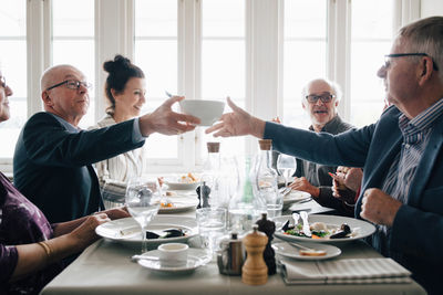 Senior male and female friends sitting for lunch by table at restaurant