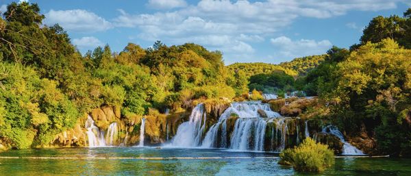 Scenic view of waterfall in forest against sky during autumn