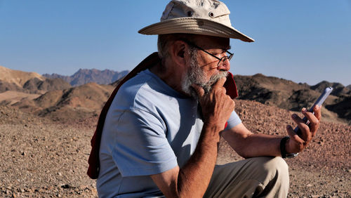 Side view of senior man using mobile phone in the desert 