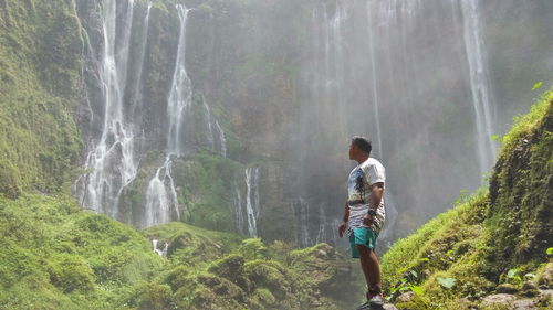 Rear view of man looking at waterfall in forest