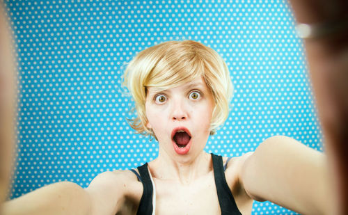 Portrait of shocked woman against blue curtain