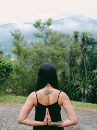 Rear view of woman sitting against trees