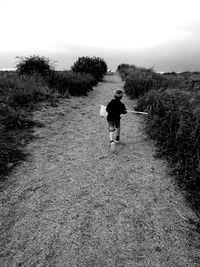 Rear view of man walking on field against sky