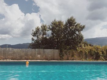 Swimming pool by trees against sky